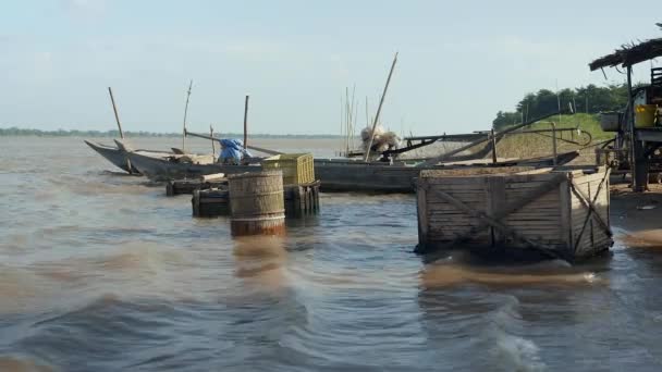 Fából készült hal rekeszek mellett kis halászhajók a river's edge egy szeles napon (közelről ) — Stock videók
