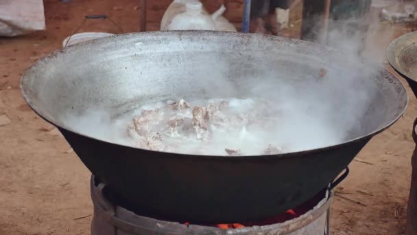 Schweinekoteletts, die in einem großen Topf über einer provisorischen Feuerstelle sieden (Nahaufnahme ) — Stockvideo
