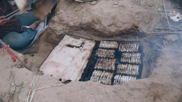 Барбекю в земле с рыбным грилем и с использованием щипцов для приготовления пищи (крупным планом  ) — стоковое видео