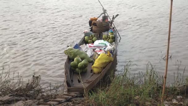 Маленькая деревянная лодка, привязанная к берегу реки и загруженная пучками зеленых кокосов, пищевых пакетов и корзин — стоковое видео