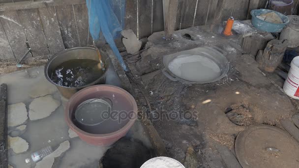 Dentro de un taller de fideos de arroz con agua hirviendo sobre fogones en el suelo. Hombre añadiendo virutas de madera para mantener el fuego — Vídeos de Stock