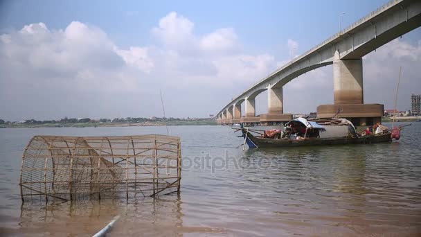 Невеликий дерев'яний рибальський човен на річці поруч з мостом; традиційна пастка для бамбукових риб на передньому плані — стокове відео