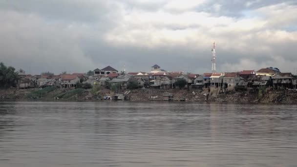 Casas de zancos de la aldea en la orilla del río en la marea baja bajo el cielo nublado oscuro (disparado desde un barco en movimiento ) — Vídeos de Stock