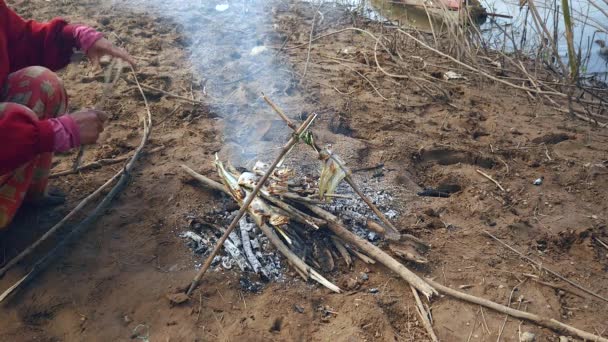 Close up de uma mulher adicionando pequenos ramos para manter o fogo aberto queimando sob peixe grelhando — Vídeo de Stock