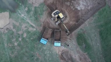 Dünya'ya iki kamyonet yükleme ve siteden bırakarak bir ekskavatör havadan görünümü 