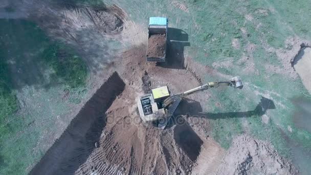 Vista estática aérea de una excavadora cargando tierra en un pequeño camión y saliendo del sitio — Vídeo de stock