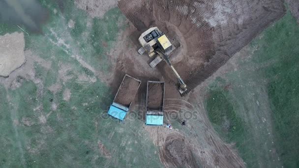 Vista aérea de una excavadora cargando tierra en dos camiones pequeños y saliendo del sitio — Vídeo de stock