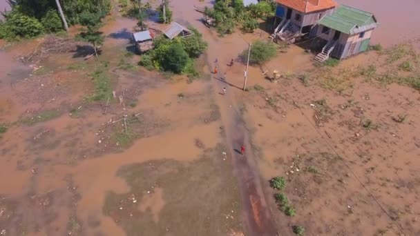 Aérea: sobrevuele a las familias que caminan por un sendero inundado que conduce a sus casas rurales — Vídeo de stock