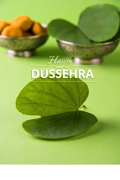 Tarjeta de felicitación diciendo feliz vijayadashmi o dussehra feliz, dussehra festival indio, mostrando apta hoja o Bauhinia racemosa con dulces tradicionales indios pedha en tazón de plata — Foto de Stock