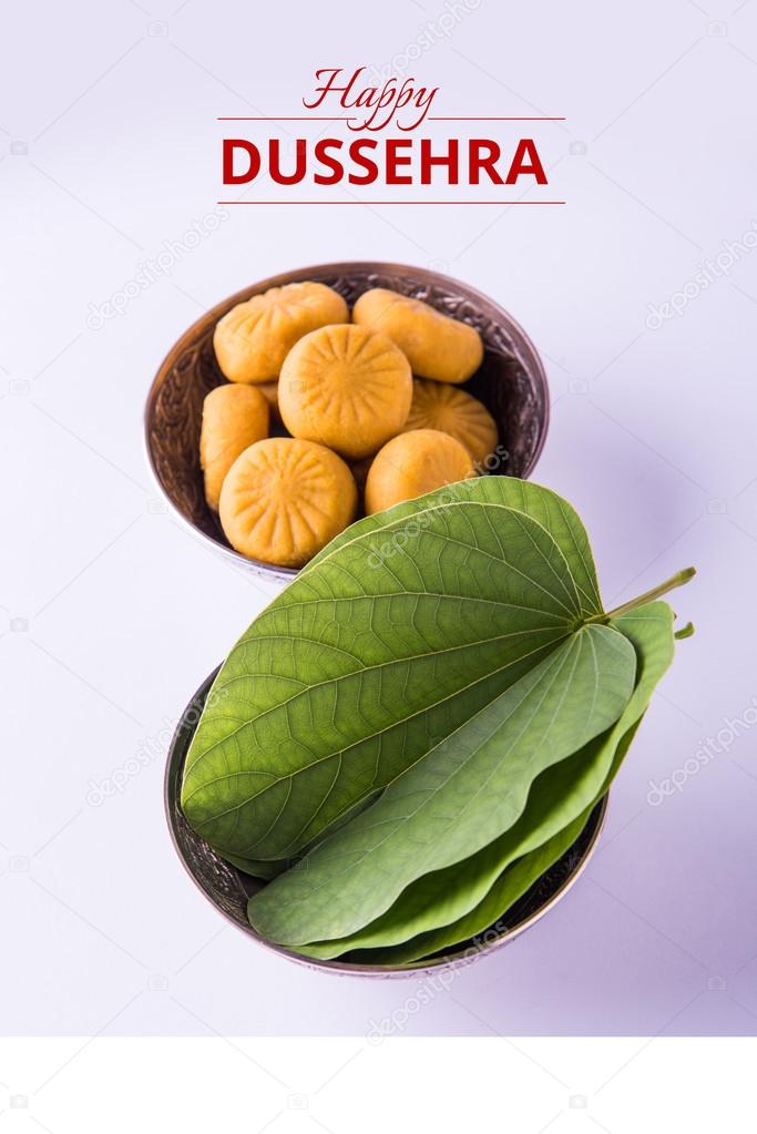 greeting card saying happy vijayadashmi or happy dussehra, indian festival dussehra, showing apta leaf or Bauhinia racemosa with traditional indian sweets pedha in silver bowl
