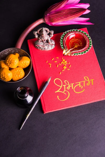 An auspicious Indian writing Shubha Labh means 'Goodness' & 'Wealth', over Red accounting note book / 'bahi khata' with goddess Laxmi, diya, sweets and lotus and pen with ink on laxmi pujan, on diwali — Stock Photo, Image