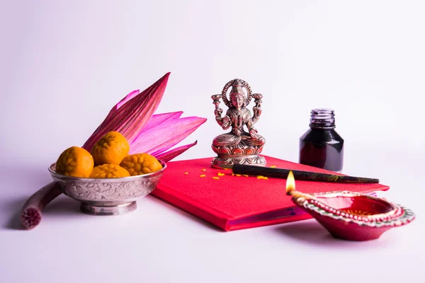 An auspicious Indian writing Shubha Labh means 'Goodness' & 'Wealth', over Red accounting note book / 'bahi khata' with goddess Laxmi, diya, sweets and lotus and pen with ink on laxmi pujan, on diwali — Stock Photo, Image