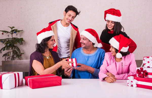 christmas time, Happy indian family sitting across table and exchanging christmas gifts wearing santa hat/cap, merry Christmas, indian family celebrating christmas
