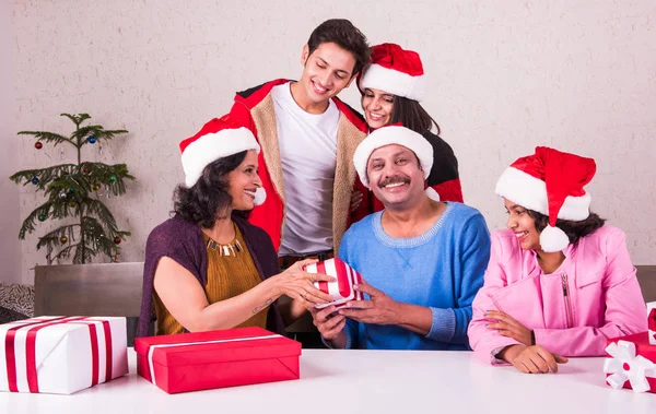 christmas time, Happy indian family sitting across table and exchanging christmas gifts wearing santa hat/cap, merry Christmas, indian family celebrating christmas