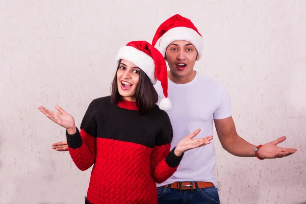 Young smiling indian man and woman with santa hat in the presentation pose, on white background, indian couple showing christmas offers or surprised with both hands stretched open