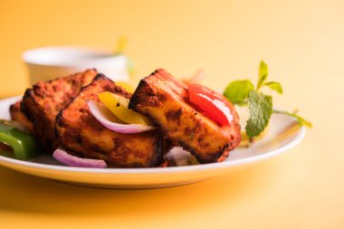 Paneer Tikka veya acı biber kebabı - Tandır Hint peyniri şişleri, beyaz tabakta servis edilir renkli kapsiyum, soğan ve yeşil sos ile