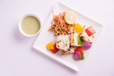 Paneer tikka kebap - tandır Hint peyniri şişleri ya da yeşil soslu beyaz tabakta servis edilen kırmızı biber paneer ve renkli salata, seçici odaklı