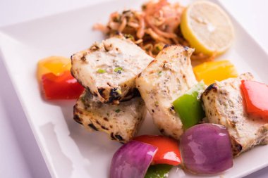 Paneer tikka kebap - tandır Hint peyniri şişleri ya da yeşil soslu beyaz tabakta servis edilen kırmızı biber paneer ve renkli salata, seçici odaklı