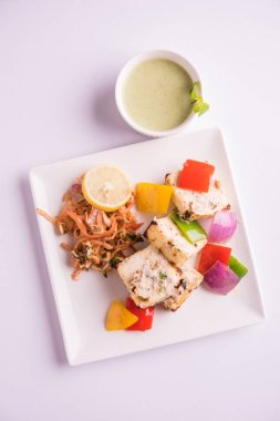 Paneer tikka kebap - tandır Hint peyniri şişleri ya da yeşil soslu beyaz tabakta servis edilen kırmızı biber paneer ve renkli salata, seçici odaklı