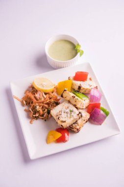 Paneer tikka kebap - tandır Hint peyniri şişleri ya da yeşil soslu beyaz tabakta servis edilen kırmızı biber paneer ve renkli salata, seçici odaklı