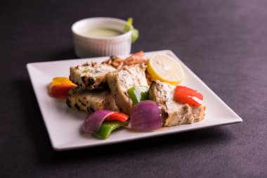 Paneer tikka kebap - tandır Hint peyniri şişleri ya da yeşil soslu beyaz tabakta servis edilen kırmızı biber paneer ve renkli salata, seçici odaklı