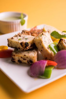 Paneer tikka kebap - tandır Hint peyniri şişleri ya da yeşil soslu beyaz tabakta servis edilen kırmızı biber paneer ve renkli salata, seçici odaklı