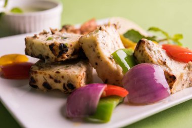 Paneer tikka kebap - tandır Hint peyniri şişleri ya da yeşil soslu beyaz tabakta servis edilen kırmızı biber paneer ve renkli salata, seçici odaklı