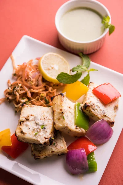 Paneer tikka kebap - tandır Hint peyniri şişleri ya da yeşil soslu beyaz tabakta servis edilen kırmızı biber paneer ve renkli salata, seçici odaklı