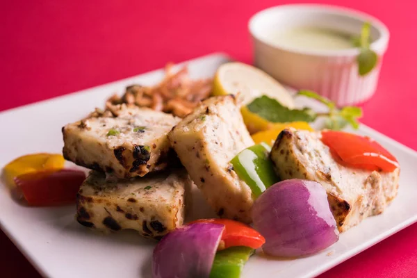 Paneer tikka kebap - tandır Hint peyniri şişleri ya da yeşil soslu beyaz tabakta servis edilen kırmızı biber paneer ve renkli salata, seçici odaklı