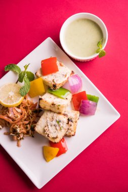 Paneer tikka kebap - tandır Hint peyniri şişleri ya da yeşil soslu beyaz tabakta servis edilen kırmızı biber paneer ve renkli salata, seçici odaklı