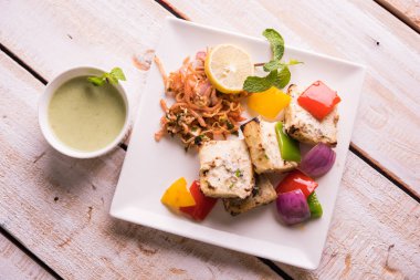 Paneer tikka kebap - tandır Hint peyniri şişleri ya da yeşil soslu beyaz tabakta servis edilen kırmızı biber paneer ve renkli salata, seçici odaklı