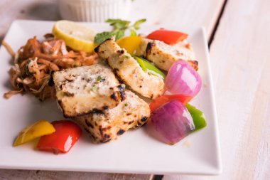 Paneer tikka kebap - tandır Hint peyniri şişleri ya da yeşil soslu beyaz tabakta servis edilen kırmızı biber paneer ve renkli salata, seçici odaklı