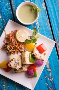 Paneer tikka kebap - tandır Hint peyniri şişleri ya da yeşil soslu beyaz tabakta servis edilen kırmızı biber paneer ve renkli salata, seçici odaklı