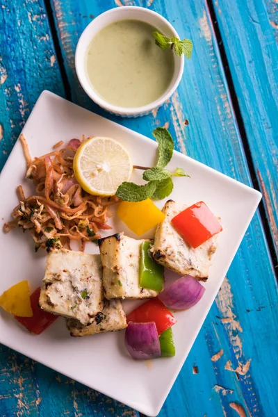 Paneer tikka kebap - tandır Hint peyniri şişleri ya da yeşil soslu beyaz tabakta servis edilen kırmızı biber paneer ve renkli salata, seçici odaklı