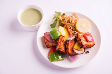 Paneer Tikka veya acı biber kebabı - Tandır Hint peyniri şişleri, beyaz tabakta servis edilir renkli kapsiyum, soğan ve yeşil sos ile