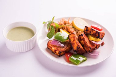 Paneer Tikka veya acı biber kebabı - Tandır Hint peyniri şişleri, beyaz tabakta servis edilir renkli kapsiyum, soğan ve yeşil sos ile