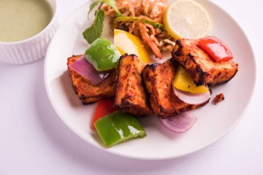 Paneer Tikka veya acı biber kebabı - Tandır Hint peyniri şişleri, beyaz tabakta servis edilir renkli kapsiyum, soğan ve yeşil sos ile