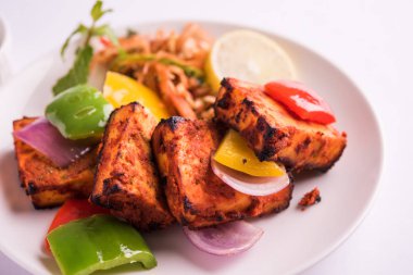 Paneer Tikka veya acı biber kebabı - Tandır Hint peyniri şişleri, beyaz tabakta servis edilir renkli kapsiyum, soğan ve yeşil sos ile