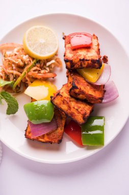 Paneer Tikka veya acı biber kebabı - Tandır Hint peyniri şişleri, beyaz tabakta servis edilir renkli kapsiyum, soğan ve yeşil sos ile