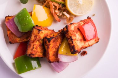 Paneer Tikka veya acı biber kebabı - Tandır Hint peyniri şişleri, beyaz tabakta servis edilir renkli kapsiyum, soğan ve yeşil sos ile
