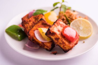 Paneer Tikka veya acı biber kebabı - Tandır Hint peyniri şişleri, beyaz tabakta servis edilir renkli kapsiyum, soğan ve yeşil sos ile