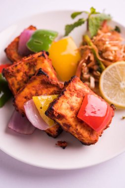 Paneer Tikka veya acı biber kebabı - Tandır Hint peyniri şişleri, beyaz tabakta servis edilir renkli kapsiyum, soğan ve yeşil sos ile