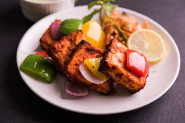 Paneer Tikka veya acı biber kebabı - Tandır Hint peyniri şişleri, beyaz tabakta servis edilir renkli kapsiyum, soğan ve yeşil sos ile