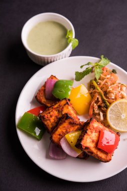 Paneer Tikka veya acı biber kebabı - Tandır Hint peyniri şişleri, beyaz tabakta servis edilir renkli kapsiyum, soğan ve yeşil sos ile