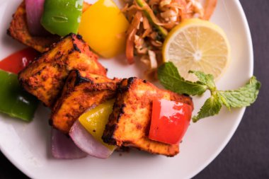 Paneer Tikka veya acı biber kebabı - Tandır Hint peyniri şişleri, beyaz tabakta servis edilir renkli kapsiyum, soğan ve yeşil sos ile