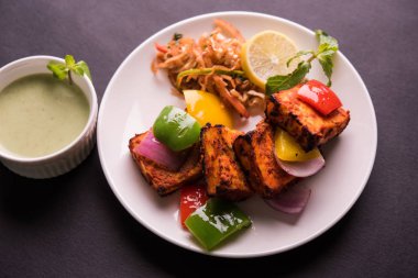 Paneer Tikka veya acı biber kebabı - Tandır Hint peyniri şişleri, beyaz tabakta servis edilir renkli kapsiyum, soğan ve yeşil sos ile