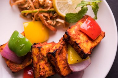Paneer Tikka veya acı biber kebabı - Tandır Hint peyniri şişleri, beyaz tabakta servis edilir renkli kapsiyum, soğan ve yeşil sos ile