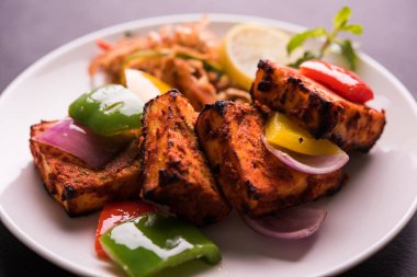Paneer Tikka veya acı biber kebabı - Tandır Hint peyniri şişleri, beyaz tabakta servis edilir renkli kapsiyum, soğan ve yeşil sos ile