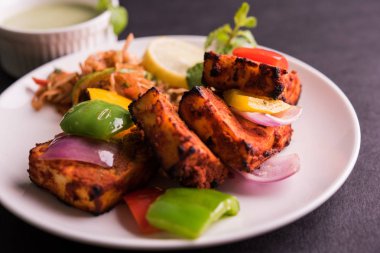 Paneer Tikka veya acı biber kebabı - Tandır Hint peyniri şişleri, beyaz tabakta servis edilir renkli kapsiyum, soğan ve yeşil sos ile