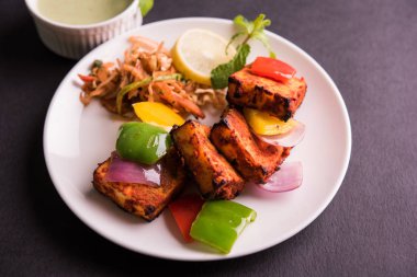 Paneer Tikka veya acı biber kebabı - Tandır Hint peyniri şişleri, beyaz tabakta servis edilir renkli kapsiyum, soğan ve yeşil sos ile